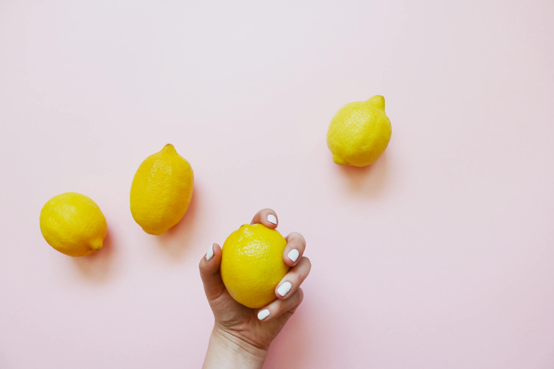 A hand holding a lemon on a soft pink background, symbolizing natural clitoral stimulation
