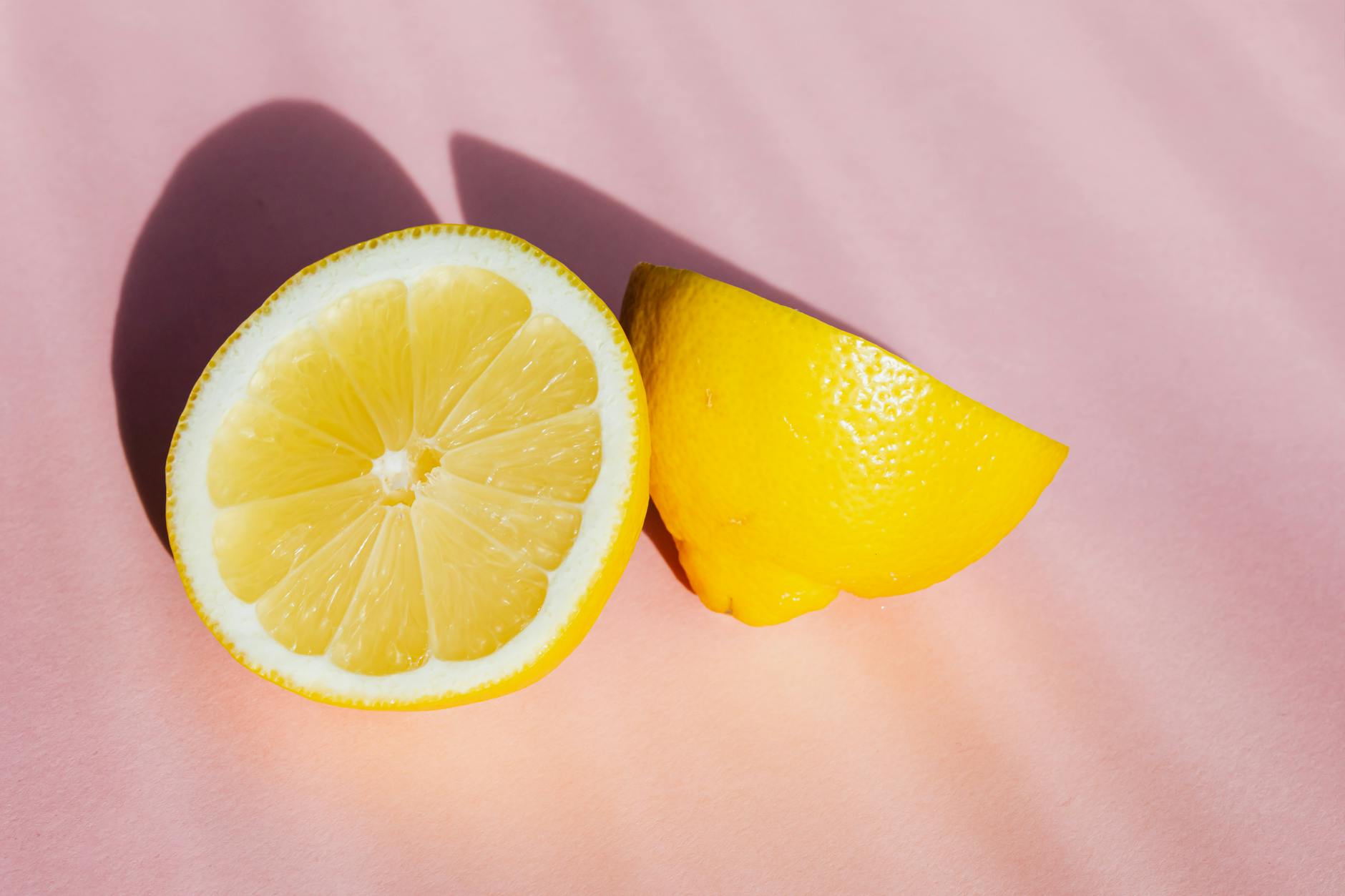 Fresh halved lemons on a pink background in sunlight