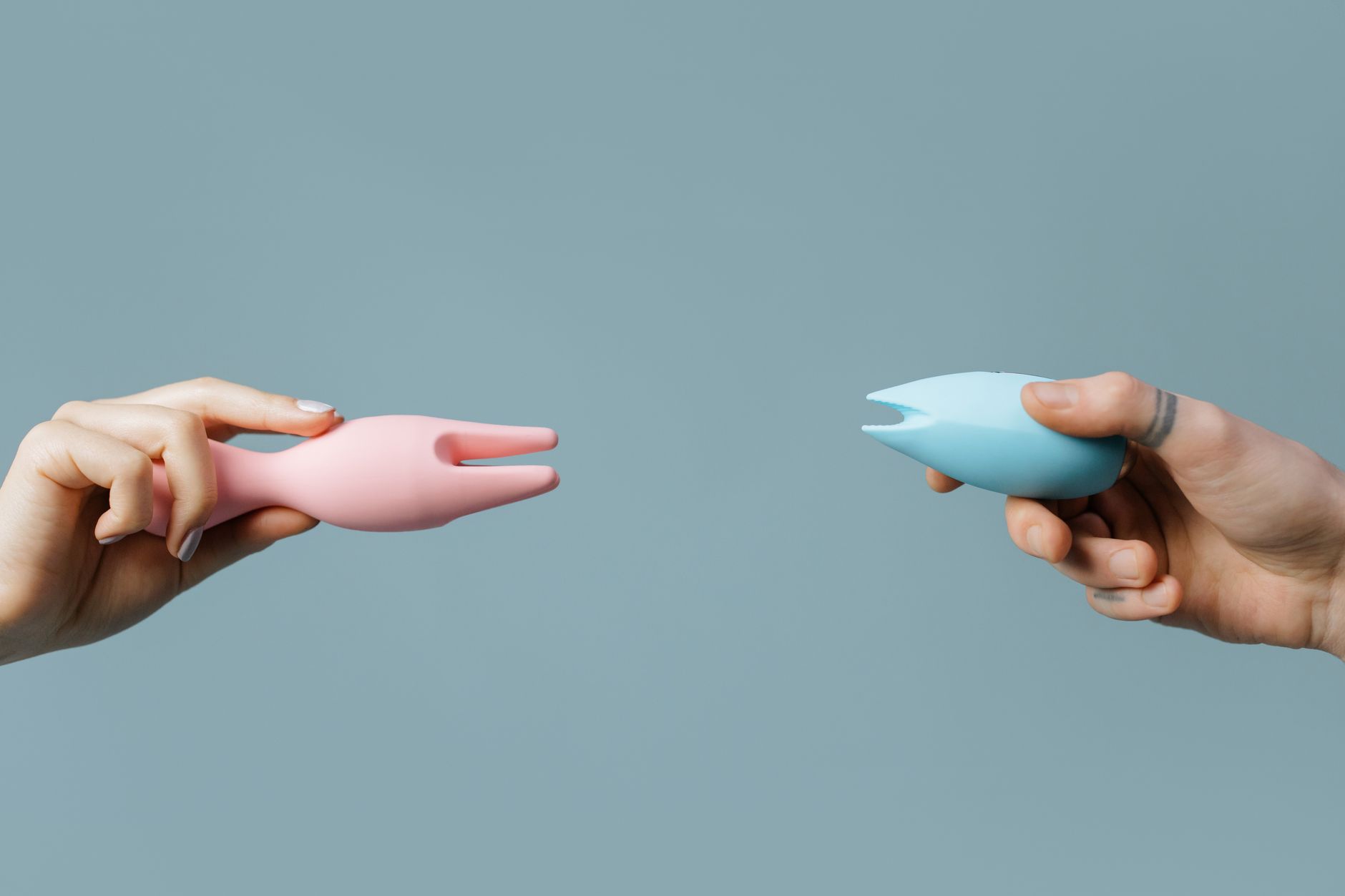 Woman holding blue and pink silicone clitoral vibrators in a contemplative moment