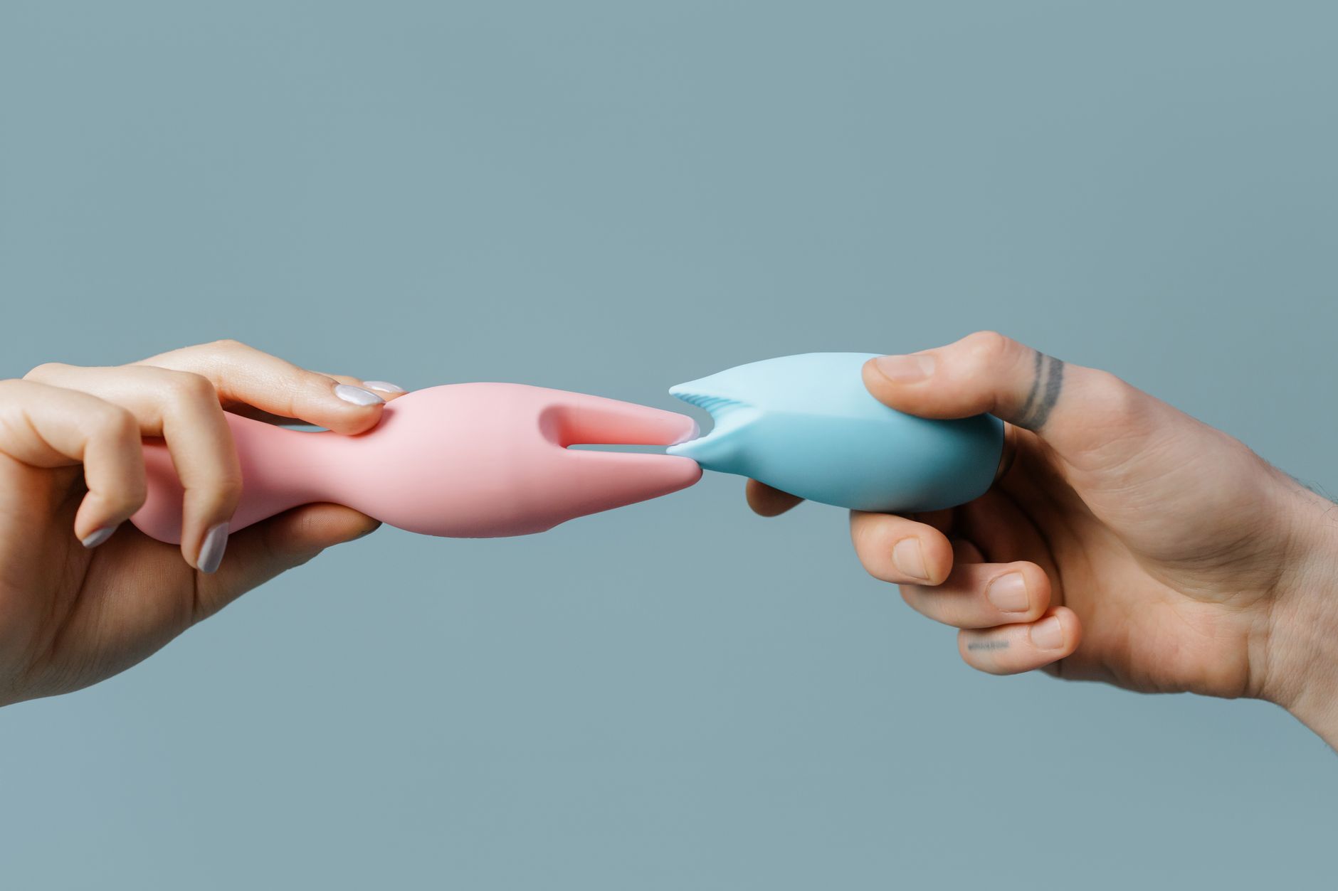 Mãos segurando um vibrador de limão rosa contra um fundo neutro