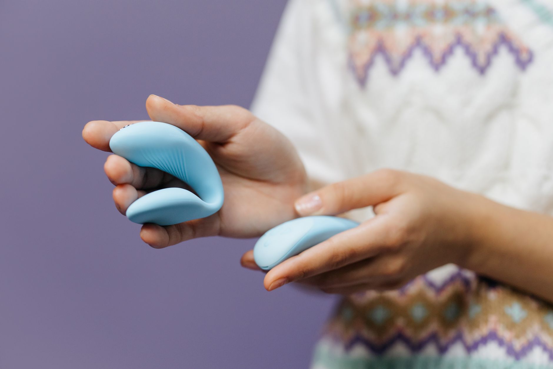 Close-up de mãos segurando um vibrador azul elegante contra um fundo roxo