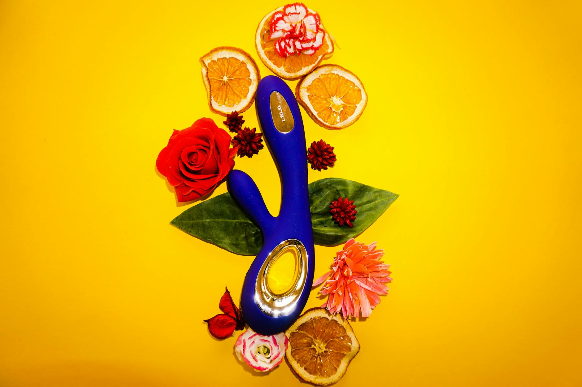 Blue lemon vibrator surrounded by flowers and citrus slices on a bright yellow background.
