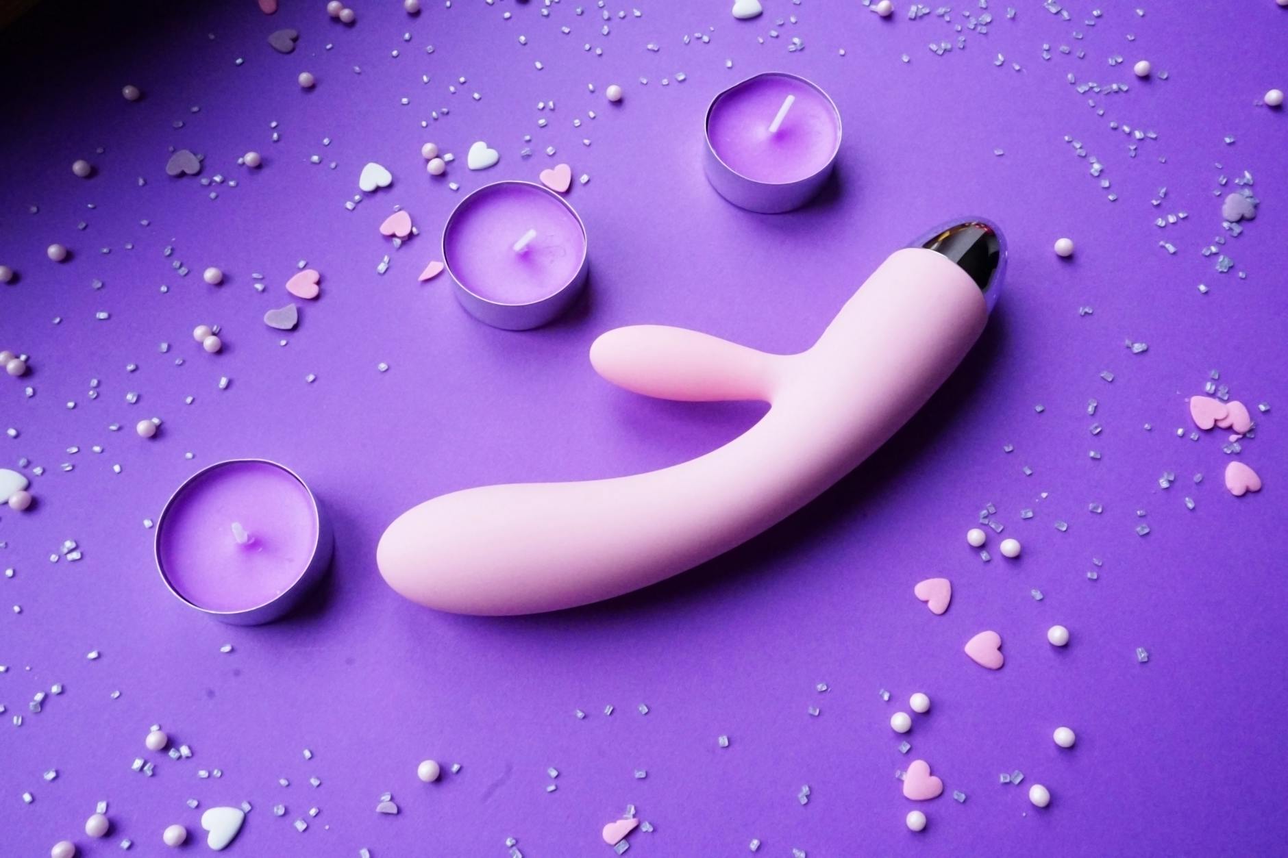 Pink vibrator on purple background with candles and confetti for couples intimacy